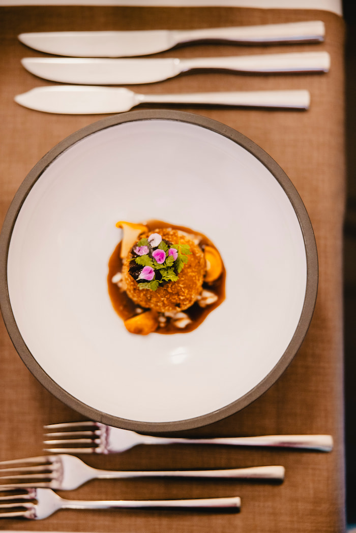 Portrait-oriented shot of culinary artistry: carefully plated dish with artistic garnishes and professional presentation on dark tableware.